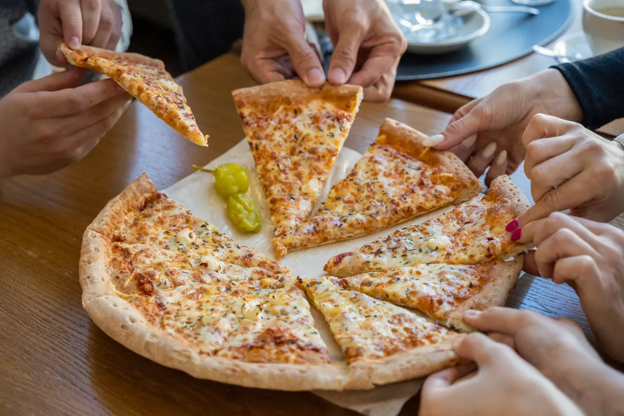 Mai multe mâini iau felii din aceeași pizza