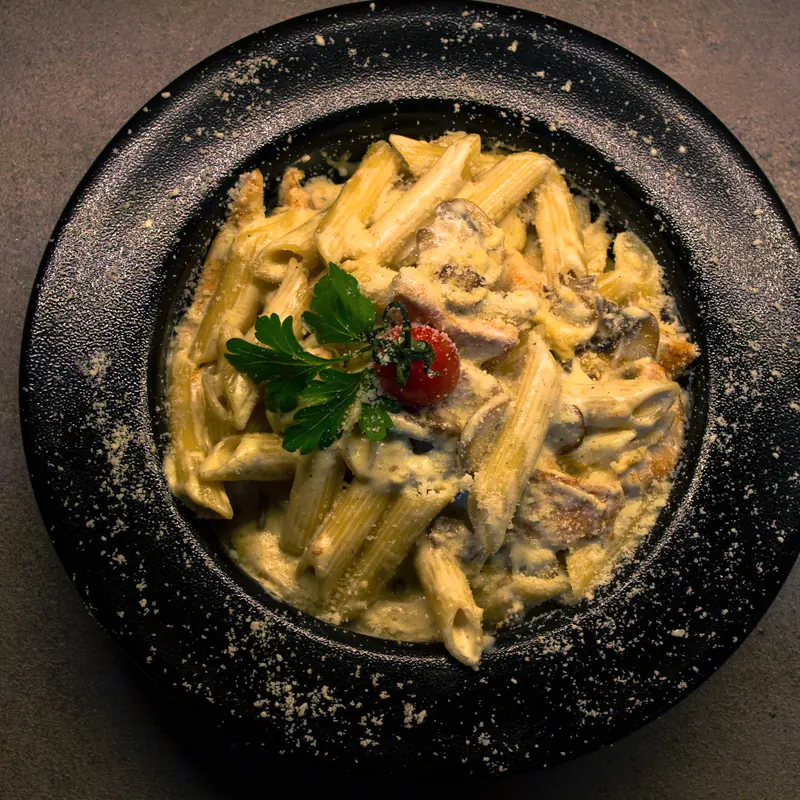 Penne în sos cremos cu ciuperci, într-un bol închis la culoare