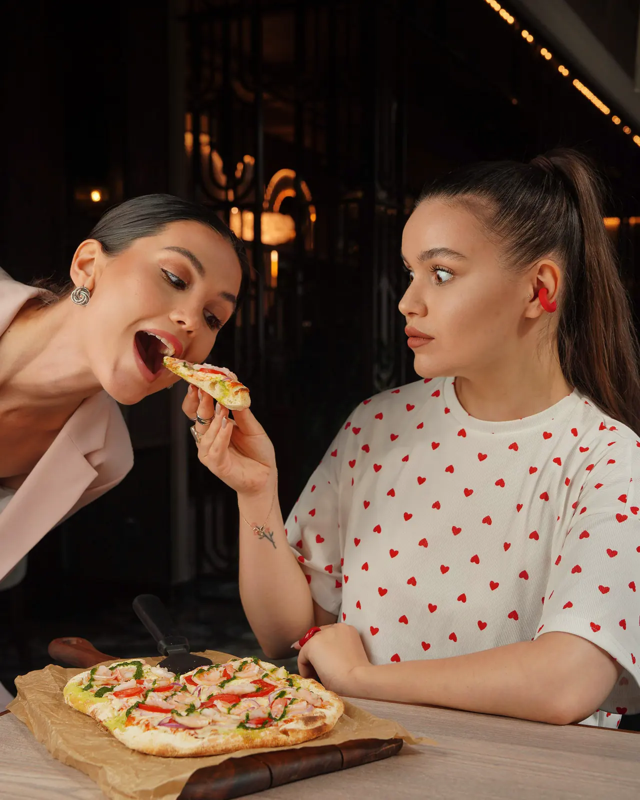 Două prietene mănâncă pizza la o masă, seara